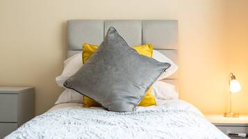 Una cama bien hecha con una colcha estampada y almohadas, una lámpara de noche y un cuadro en la pared.