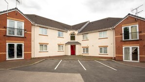 A two-story residential building with a red door, multiple windows, and a parking area in front. - Apartment 4 (Worksop)