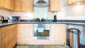 A modern kitchen with wooden cabinets, a stainless steel stove, a microwave, and a trash bin. - Apartment 4 (Worksop)