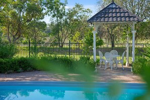 A gazebo with a tiled roof, surrounded by a white fence, and a pool in the foreground.