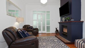 Una sala de estar con chimenea, sofá de cuero y televisor montado en la pared.