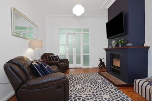 Un salon avec une cheminée, un canapé en cuir et un téléviseur fixé au mur.