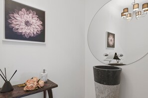 Une salle de bain avec un grand miroir, un lavabo, un vase de fleurs et un tableau encadré au mur.