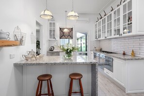 Une cuisine moderne dotée d’un grand îlot central, de luminaires suspendus et de meubles de cuisine blancs.