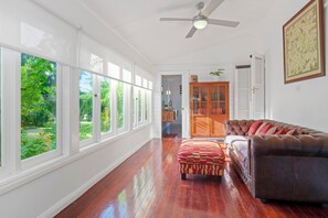A spacious room with a large window, a ceiling fan, a leather sofa, and a wooden cabinet.