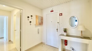A hotel hallway with a white door, a fire alarm, a mirror, and a small plant on a counter. - Tália XI - Near the beach - Vilamoura (Vilamoura)