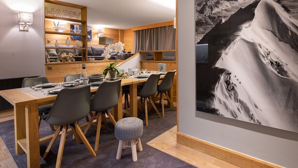 Un comedor con una mesa y sillas de madera, un taburete pequeño y un estante de pared con objetos decorativos.