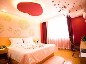Une chambre d’hôtel avec un lit, une table de chevet, un mur d’accent rouge et une grande fenêtre avec des rideaux.