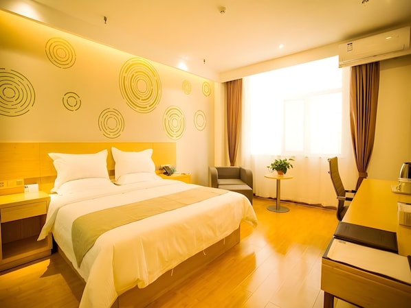 Une chambre d’hôtel avec un grand lit, un bureau et une chaise. Les murs sont décorés de motifs et il y a une fenêtre avec des rideaux.