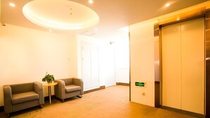 A hotel lobby with two sofas, a small table with a plant, a large circular ceiling light, and an elevator. - Greentree Inn Jinzhong Yuci Old Town (Jinzhong)