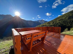 A wooden deck with a bench overlooking a mountainous landscape under a clear sky.