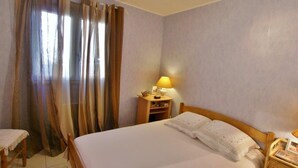 Una camera da letto con un letto, un comodino con una lampada, una sedia e una finestra con tende.