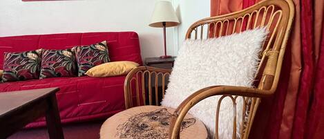 En stue med en rød sofa, en træstol med sæde af træstamme, en lampe og et billede i ramme på væggen.