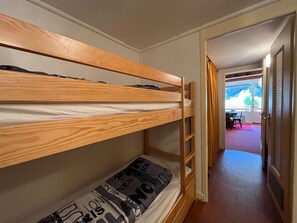 A bunk bed room with a wooden ladder, a window with curtains, and a door leading to another room.