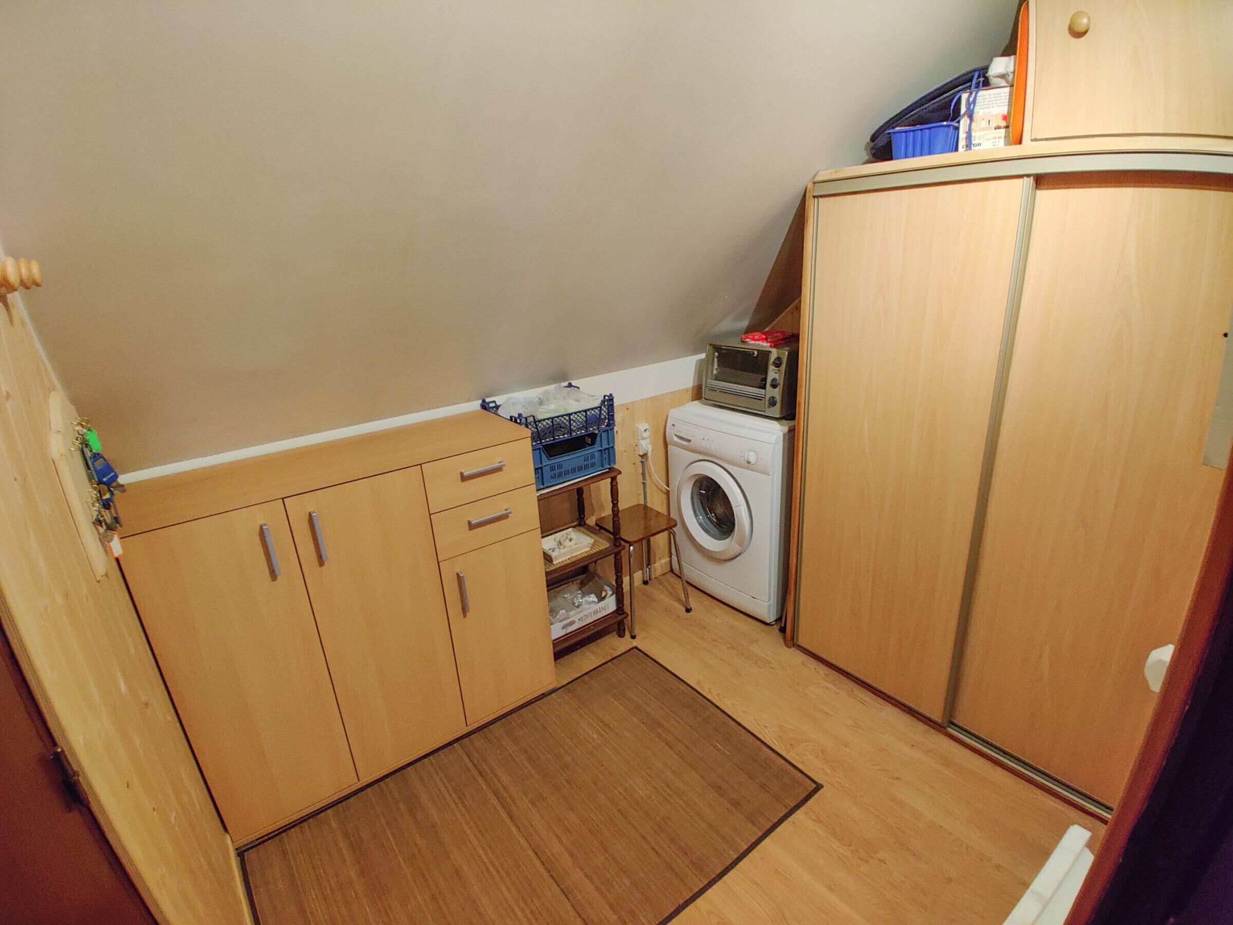 A compact laundry room with a washing machine, a drying rack, and wooden cabinets.