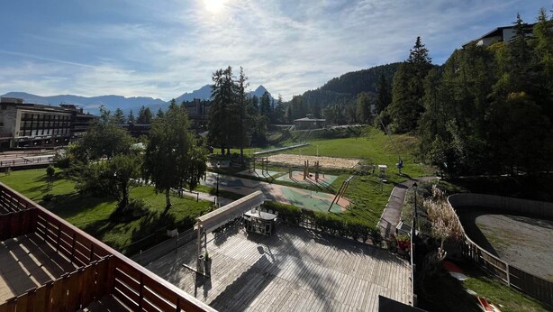 A view of a sports field with a wooden deck and seating area, surrounded by trees and buildings. - Spacious renovated T4 for 8 at Pra Loup 1600 (Pra-Loup)