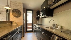 A modern kitchen with dark cabinetry, stainless steel appliances, and a large clock on the wall. - Spacious renovated T4 for 8 at Pra Loup 1600 (Pra-Loup)