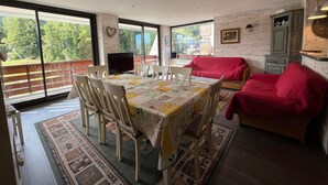 A dining area with a table set for four, a red sofa, and a TV on a stand. - Spacious renovated T4 for 8 at Pra Loup 1600 (Pra-Loup)