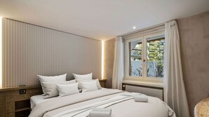 Un dormitorio moderno con una cama grande, una mesita de noche de madera, una ventana con cortinas y vistas al verdor exterior.