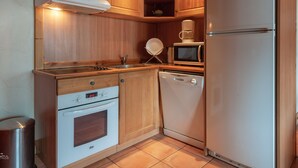 Una cocina compacta con armarios de madera, lavavajillas blanco, microondas y refrigerador.