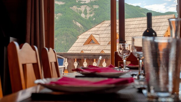 Una mesa de comedor con platos, vasos y una botella, con vistas a la montaña a través de una ventana.