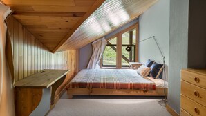 Une chambre avec un plafond en pente, un lit recouvert d’une couvre-lit à motifs, un bureau et une commode.