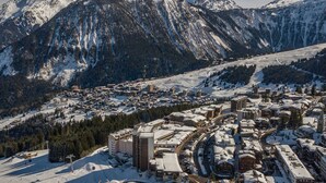 Une ville de montagne enneigée, avec un ensemble de bâtiments principaux au centre, des pistes de ski et, en arrière-plan, des montagnes escarpées.