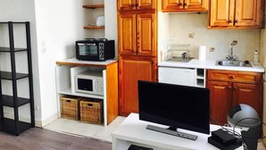 Een compacte keuken met houten kastjes, een magnetron, een fornuis en een televisie op een witte tafel.