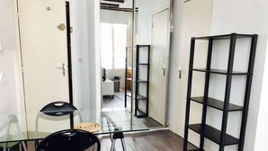Een kamer met een glazen tafel, twee stoelen, een zwart kastenmeubel en een deur naar een andere kamer.