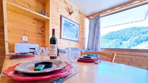 A wooden cabin dining area with a table set for two, a bottle of wine, and a scenic mountain view. - Renovated studio at the foot of the slopes in Pra-Loup, ideal for 4 people (Pra-Loup)
