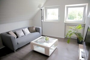 A modern living room with a grey sofa, a glass coffee table, and a potted plant. - Vacation apartment 1 - Apartments Riedel (Pegnitz)