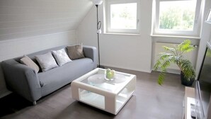 A modern living room with a grey sofa, a glass coffee table, and a potted plant. - Vacation apartment 1 - Apartments Riedel (Pegnitz)