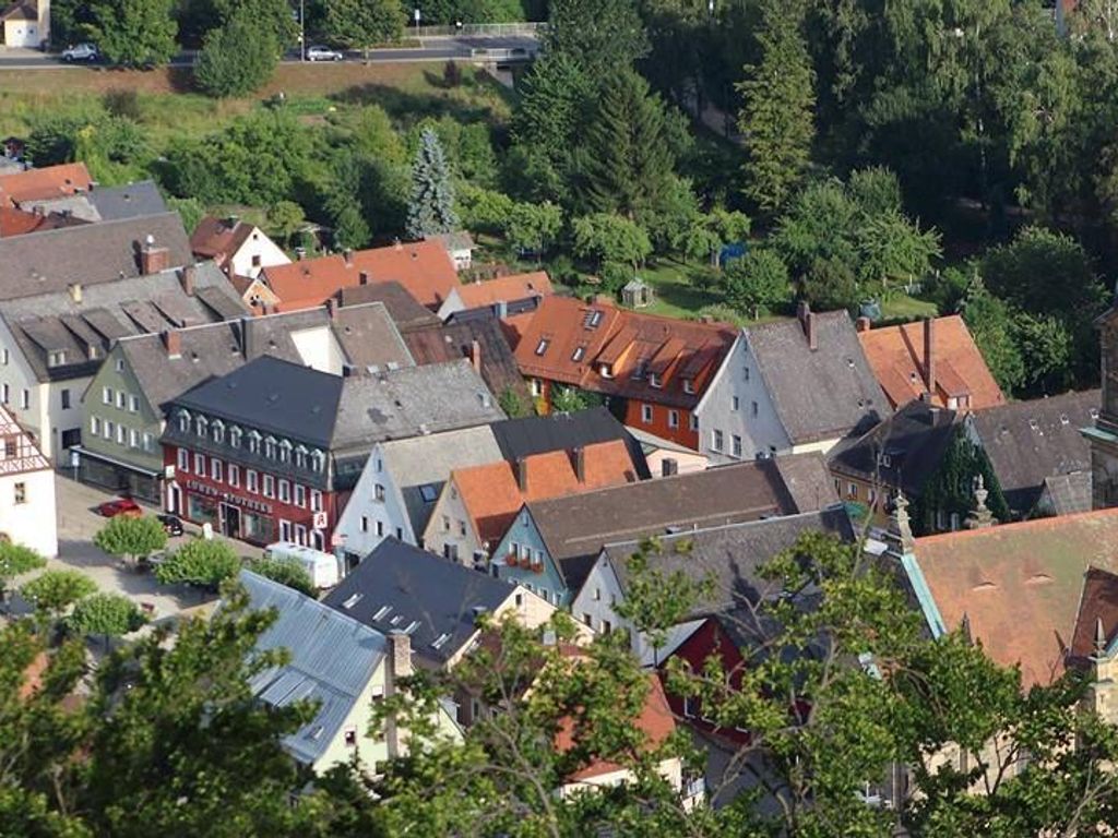Un ensemble de bâtiments de style européen traditionnel, aux toits de couleurs variées, avec une rangée d’arbres dense en arrière-plan.