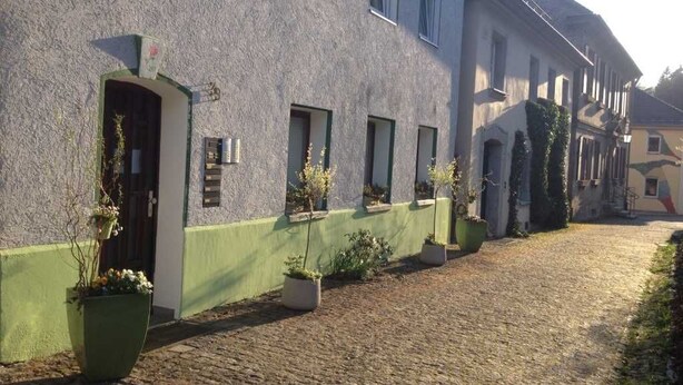 A building with a green facade, multiple windows, and potted plants along the side. - Vacation apartment 1 - Apartments Riedel (Pegnitz)
