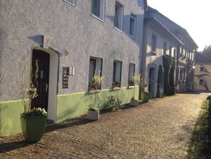A building with a green facade, multiple windows, and potted plants along the walkway.