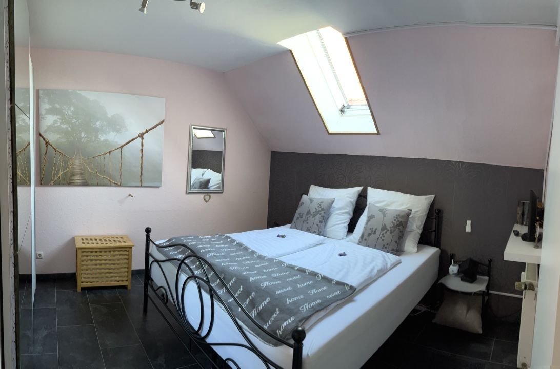 A bedroom with a bed, a bedside table, a mirror, a small stool, and a framed picture on the wall.