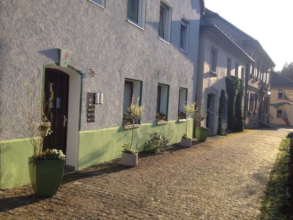 Ein Gebäude mit grüner Fassade, zahlreichen Fenstern und Blumentöpfen an der Seite.
