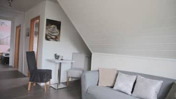 Ein stilvolles Loft-Zimmer mit grauem Sofa, einem kleinen weißen Tisch und einem schwarzen Sessel.