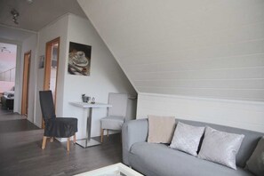 A modern loft-style room with a gray sofa, a small white table, and a black chair. - Vacation Apartment 1 - Riedel Apartments (Pegnitz)