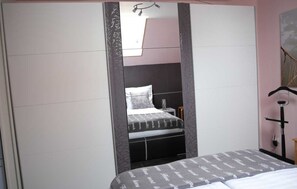 A bedroom with a bed, a nightstand, a mirror, and a wardrobe. - Vacation apartment 1 - Apartments Riedel (Pegnitz)