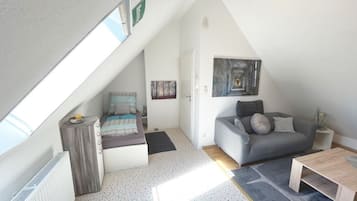 Ein Loft-Zimmer mit schrägem Dach, einem grauen Sofa, einem Holztisch und einem Bild an der Wand.