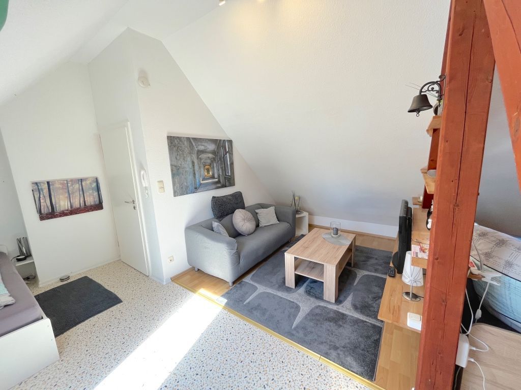 A loft-style room with a sloped ceiling, a gray sofa, a wooden coffee table, and a painting on the wall.