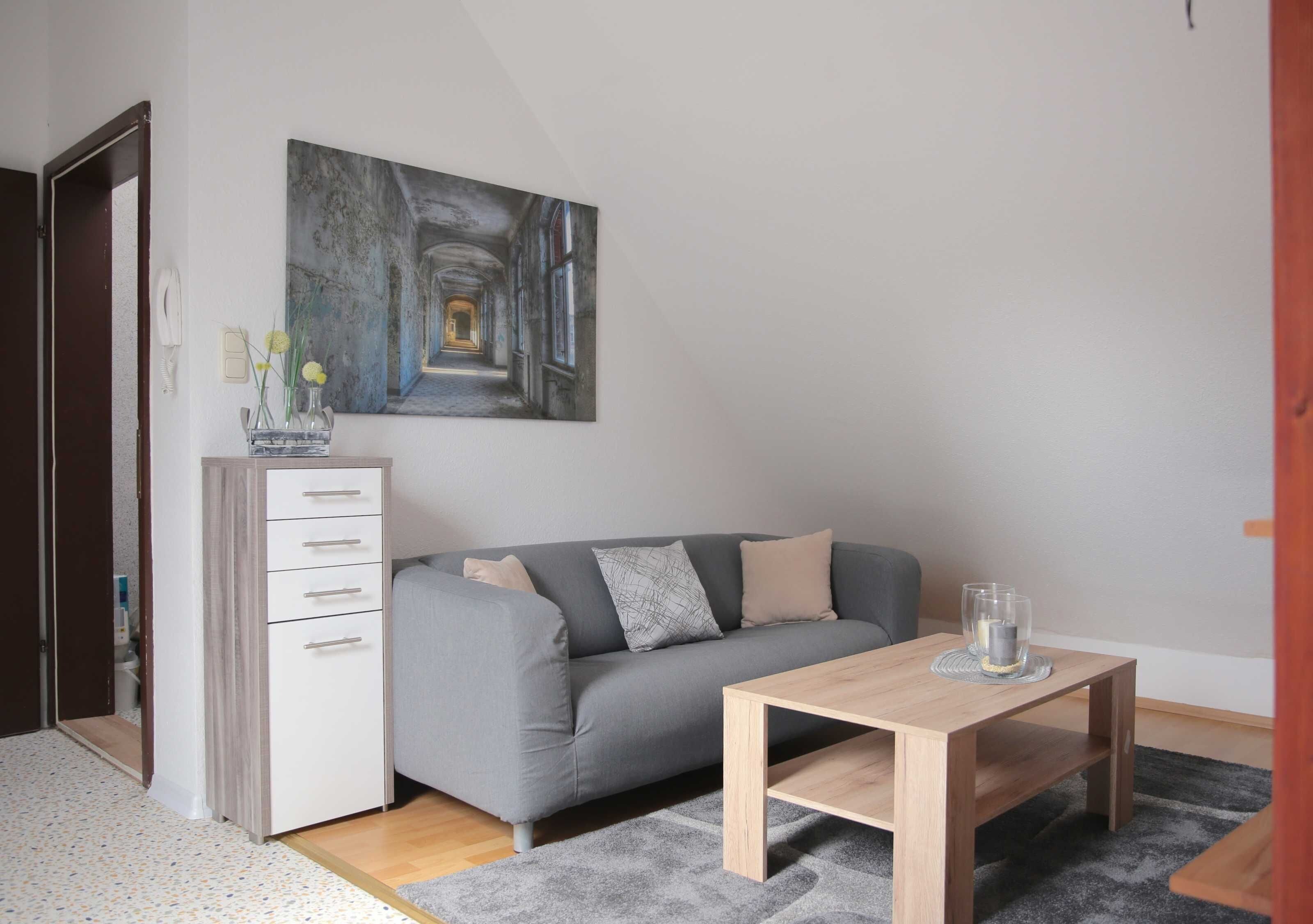 Ein modernes Wohnzimmer mit grauem Sofa, einem Holztisch und einem Bild an der Wand.