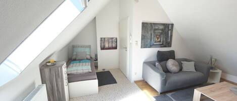 Una habitación estilo loft con techo inclinado, un sofá gris, una mesa de centro de madera y un cuadro en la pared.