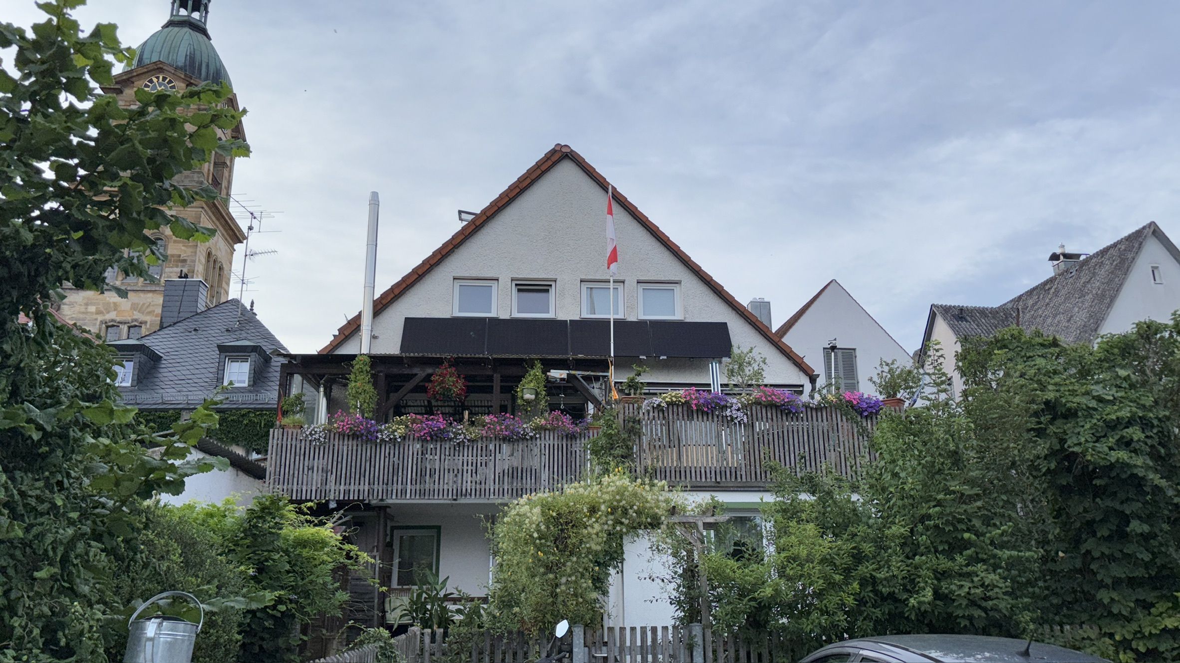 Un bâtiment à deux étages, doté d’un toit triangulaire, d’un balcon orné de fleurs et d’un drapeau.