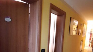 A hallway with wooden doors and a yellow wall. There are framed pictures on the wall and a plant in the corner. - Ca Barozzi (Venezia)