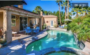 A swimming pool with a curved design, surrounded by a patio with chairs and a table, palm trees, and a clear blue sky. - Luxury Private Desert Villa with Pool, Spa & Views safe area<br>In a cul de sac <br><br> (Palm Springs)