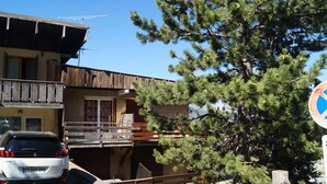 A building with a balcony, a parked car, and a pine tree.