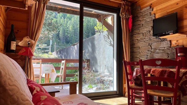 A cozy cabin room with a large sliding glass door leading to an outdoor deck, a wooden ceiling, and a stone wall.