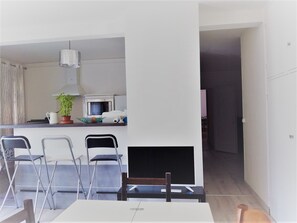 Cozinha moderna com micro-ondas, chaleira e planta em vaso. Possui área de refeições com mesa e cadeiras.